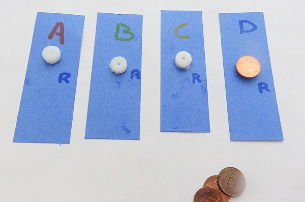 Four circular pieces of lip balm on individual paper strips are pressed down onto the paper using a penny