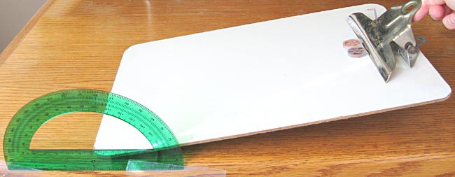 A stack of two pennies sitting on a paper towel strip are placed on a clipboard as the clipboard is raised at an angle