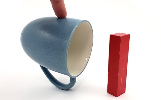 A mug is held to balance on its handle next to an upright rectangular block