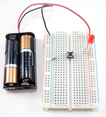 A battery pack, LED and button wired to a breadboard