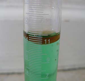 Oil settles on the top of blue colored water within a graduated cylinder