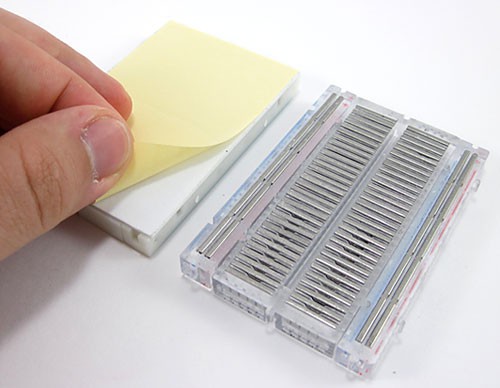 Paper is peeled off of an adhesive on the back of a breadboard