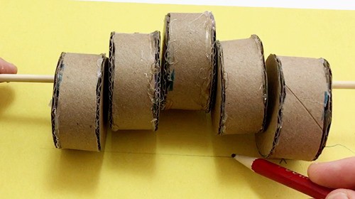 Person making a mark along a line indicating the middle of a  cylinder of a set of 5 cylinders attached to a skewer.   