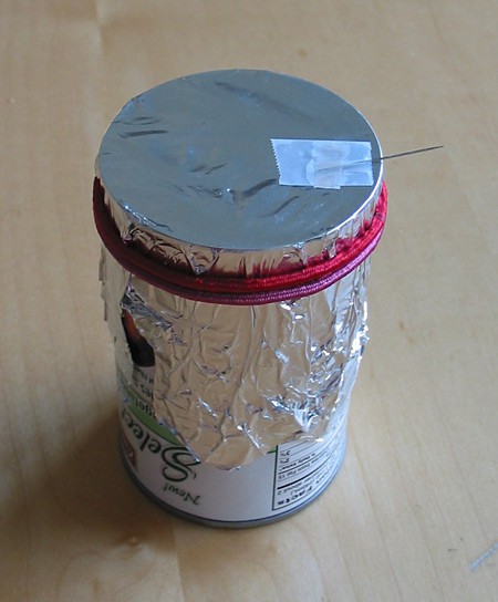 A needle is taped to aluminum foil stretched over the opening of a tin can
