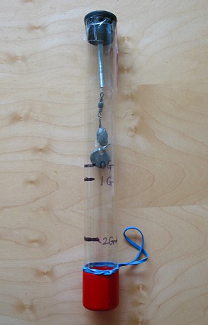 A spring attached to a rubber stopper suspends weights within a plastic tube