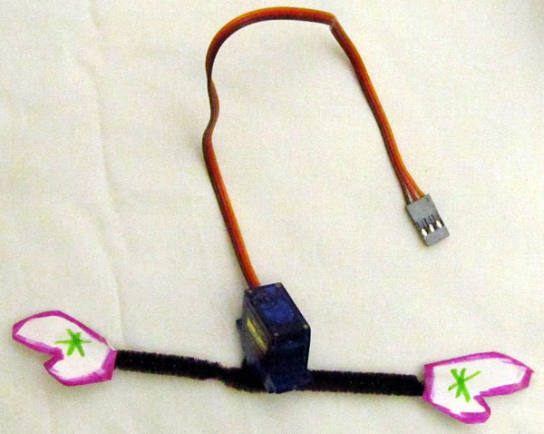 Model arms made of pipe cleaners are attached to a servo horn mounted onto a servo motor