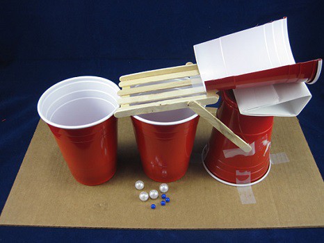 Three red solo cups set up as a base, holding up half a solo cup and a ramp made of popsicle sticks