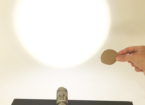 Hand holding cardboard circle next to a flashlight.
