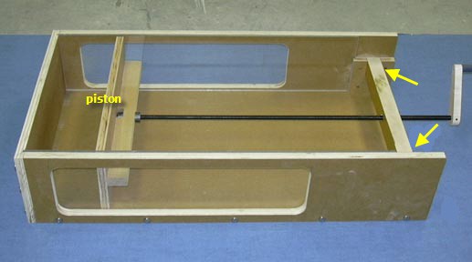 A shallow box is built with an open top and one side wall attached to a long screw