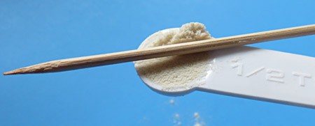 The side of a wooden skewer is used to level powder held in a measuring spoon