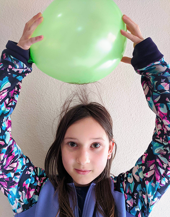 Girl rubbing a balloon on her head and hair standing up from static electricity.