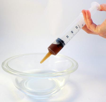 A syringe drops a sodium alginate and food solution into a bowl of calcium chloride solution