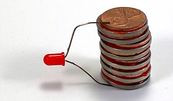A stack of coins that are part of a homeade battery and an LED that is being lit by this voltaic pile