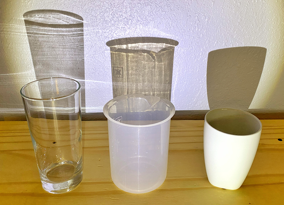 Three containers with light shining through them to demonstrate properties of being translucent, transparent, or opaque