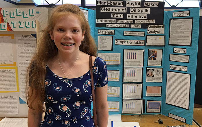 A student standing in front of a science fair display board