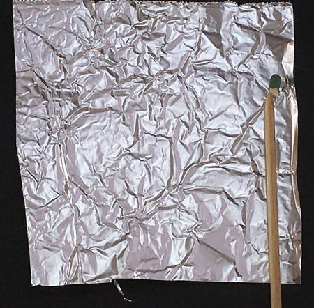  A cut skewer aligned with one side of a square piece of aluminum foil with a match at its tip and about 2 cm of space left free above the skewer and match.  
