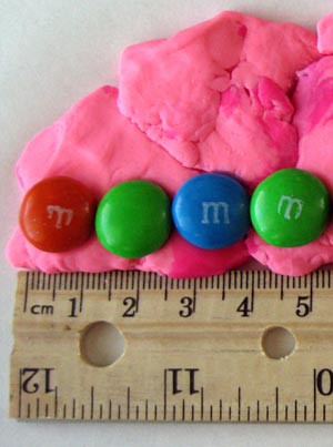 Four M&M candies are lined up on a piece of putty and measured in length