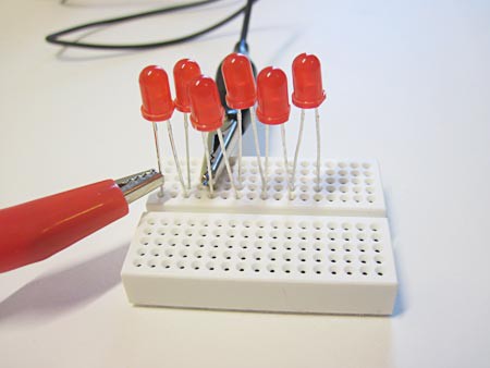 Two alligator clips connect to two different LEDs in a breadboard