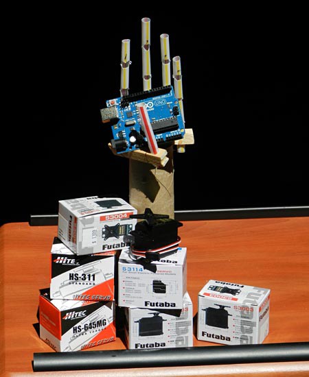 A homemade prosthetic hand holds a microprocessor board next to a servo motor