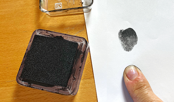 A thumb next to a pad of ink and a fingerprint