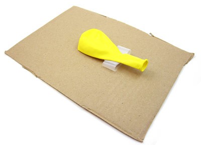 A deflated balloon taped to a rectangular cardboard sheet