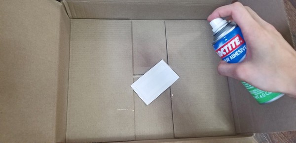 Spraying adhesive 12-15 inches away from vinyl tattoo sheet. 