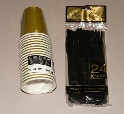 A stack of gold paper cups and a bag of black plastic knifes