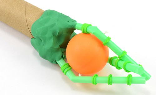 A robot hand holds a ping pong ball between fingers made of straws