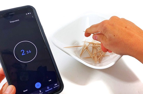  A hand reaching into a bowl filled with toothpicks. A stopwatch next to the bowl shows 2 seconds. 