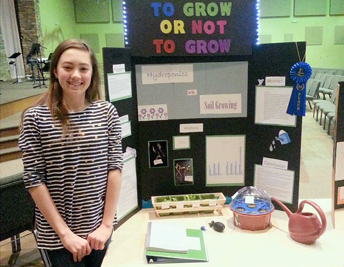 A student standing in front of a science fair display board