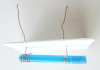 Two copper wires pushed through a styrofoam sheet are wrapped around the ends of a cut straw
