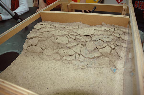 Cracks begin to form in a top layer of sand as it is compressed and pushed upward