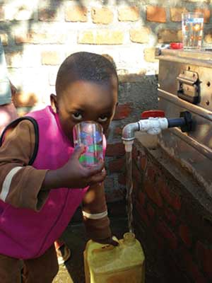 A young Rwandan boy drinks a glass of water while filling his water tank