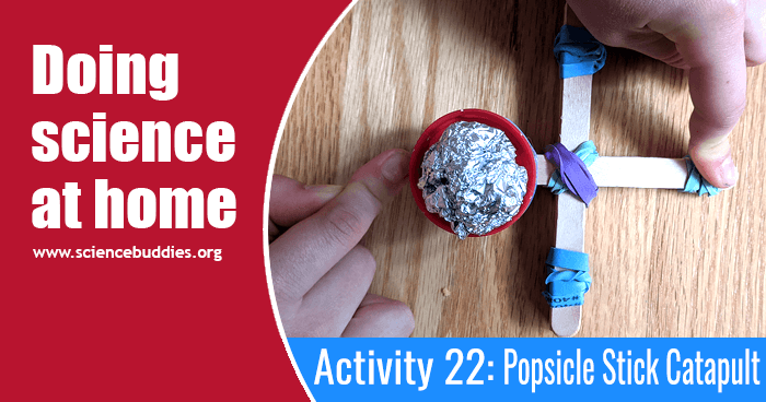 Example of a small catapult made from popsicle wooden sticks, rubber bands, and a recycled plastic lid. The catapult is holding a small aluminum foil ball.