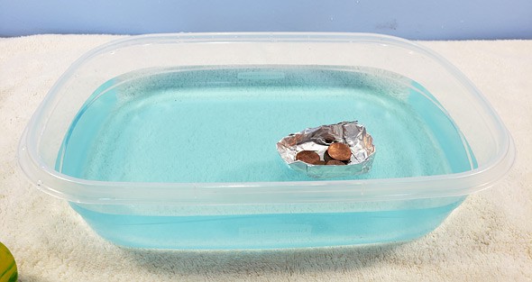 An aluminum foil boat holds pennies in a container of blue water