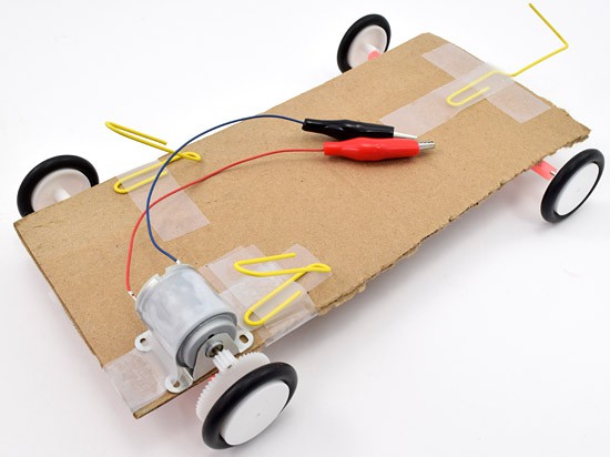 Three paper clips are bent and taped to a solar powered car chassis to help support a solar panel placed above it