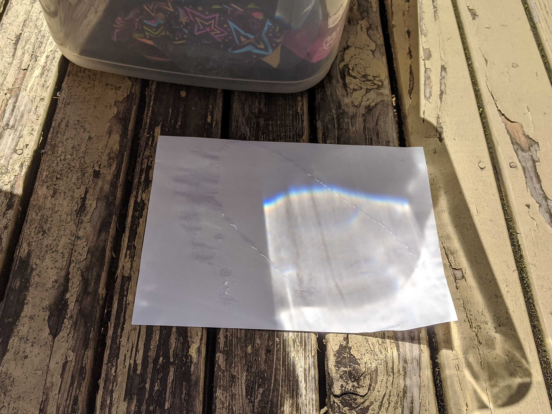 Rainbow cast on white paper through glass container of water on a sunny day