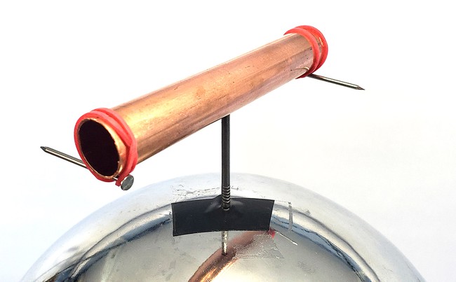 A copper pipe balanced on top of a nail, which is taped to the top of a Van de Graaff generator. The pipe has two additional nails sticking out from its ends, held in place by rubber bands, and pointed in opposite directions.