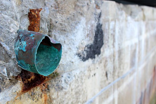 A copper pipe in a wall covered in blue rust