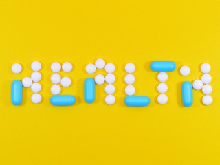 white and blue pills layed out on yellow background to spell health