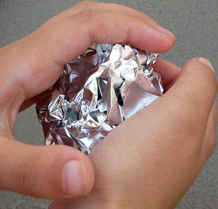 Two hands squeeze aluminum foil into a ball