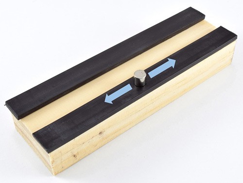 A small cylinder magnet rubs across a magnetic strip attached to a wooden block