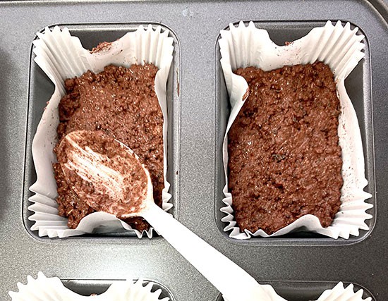  A wet, red-brown mixture filling paper muffin liners in a pan one-third full.  