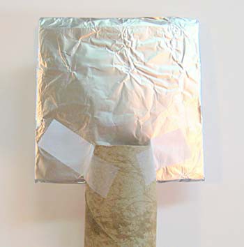 A cardboard square is wrapped in a layer of aluminum foil and is taped in slits at the end of a cardboard tube