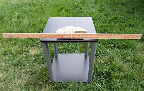 On a small table a meterstick is placed parallel to the ground and secured to a large rock