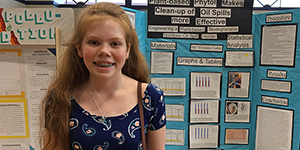 A student standing in front of a science fair display board