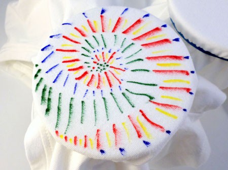 Markers are used to draw lines of different colors on a shirt in a spiral pattern