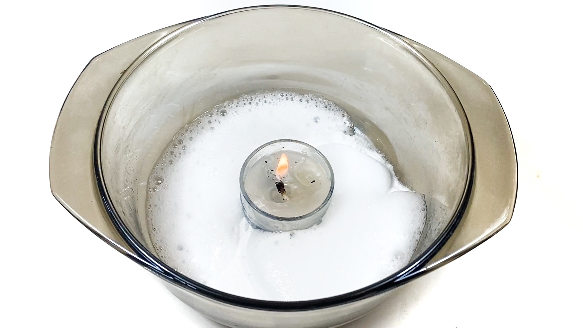 A glass bowl with a burning candle inside. Around the candle, there is white foam.