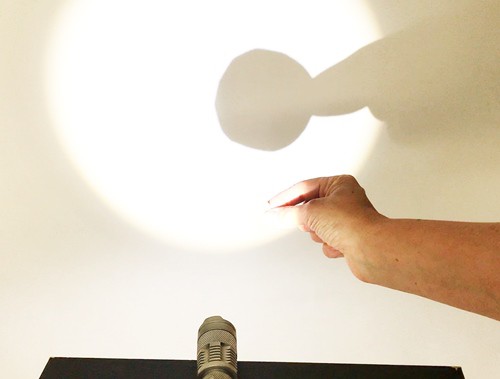 Hand holding a cardstock circle in front of a flashlight to cast a circle.