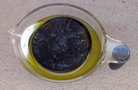 A reusable coffee filter is filled with hair and submerged in a measuring cup filled with oil and water